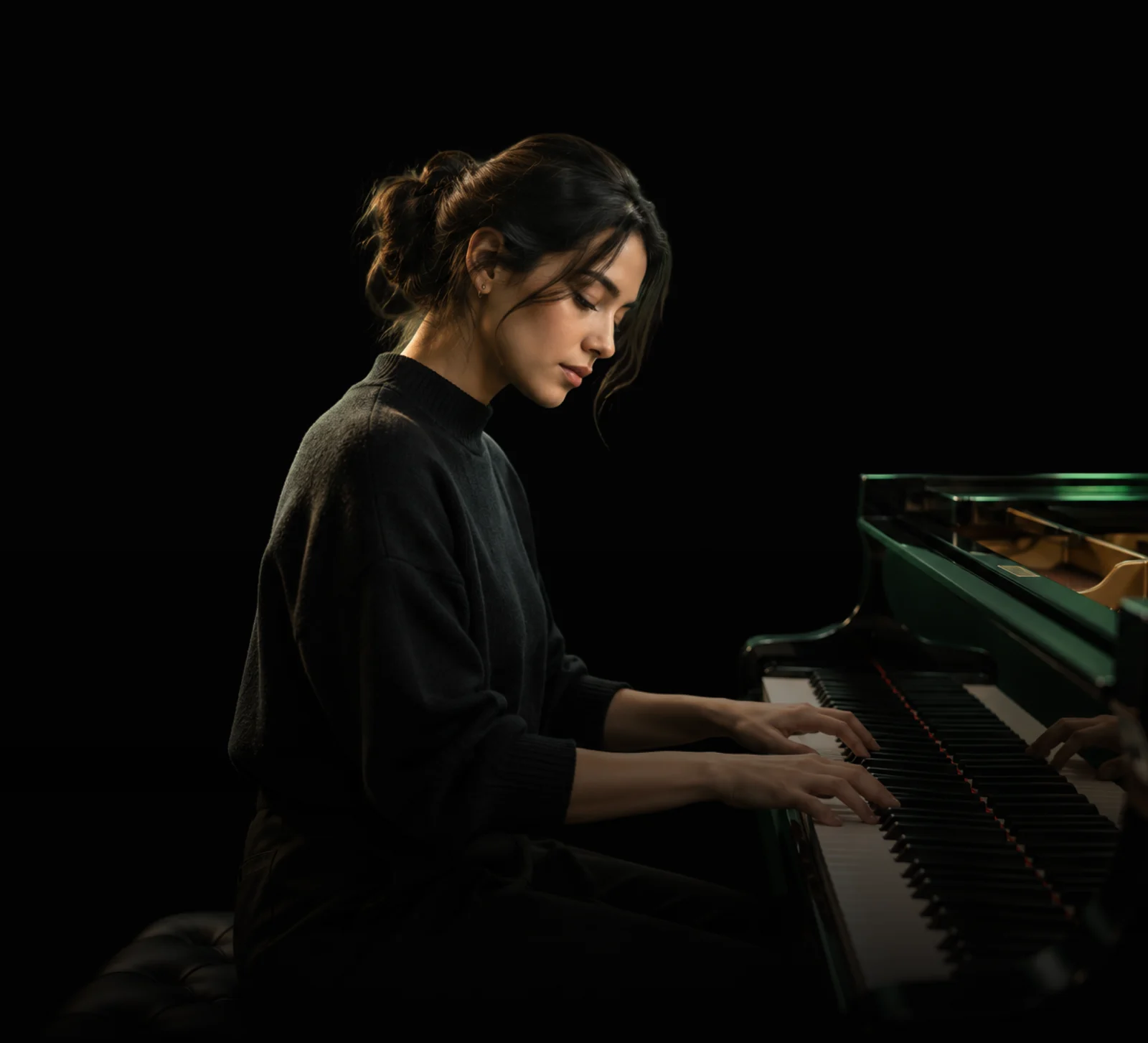 A woman with her hair in a bun playing a grand piano in a dim, warmly lit room, her hands on the keys.