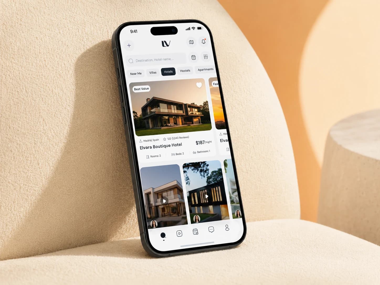 Lovo home feed with hotel listings, on a phone leaning against a cream boucle armchair